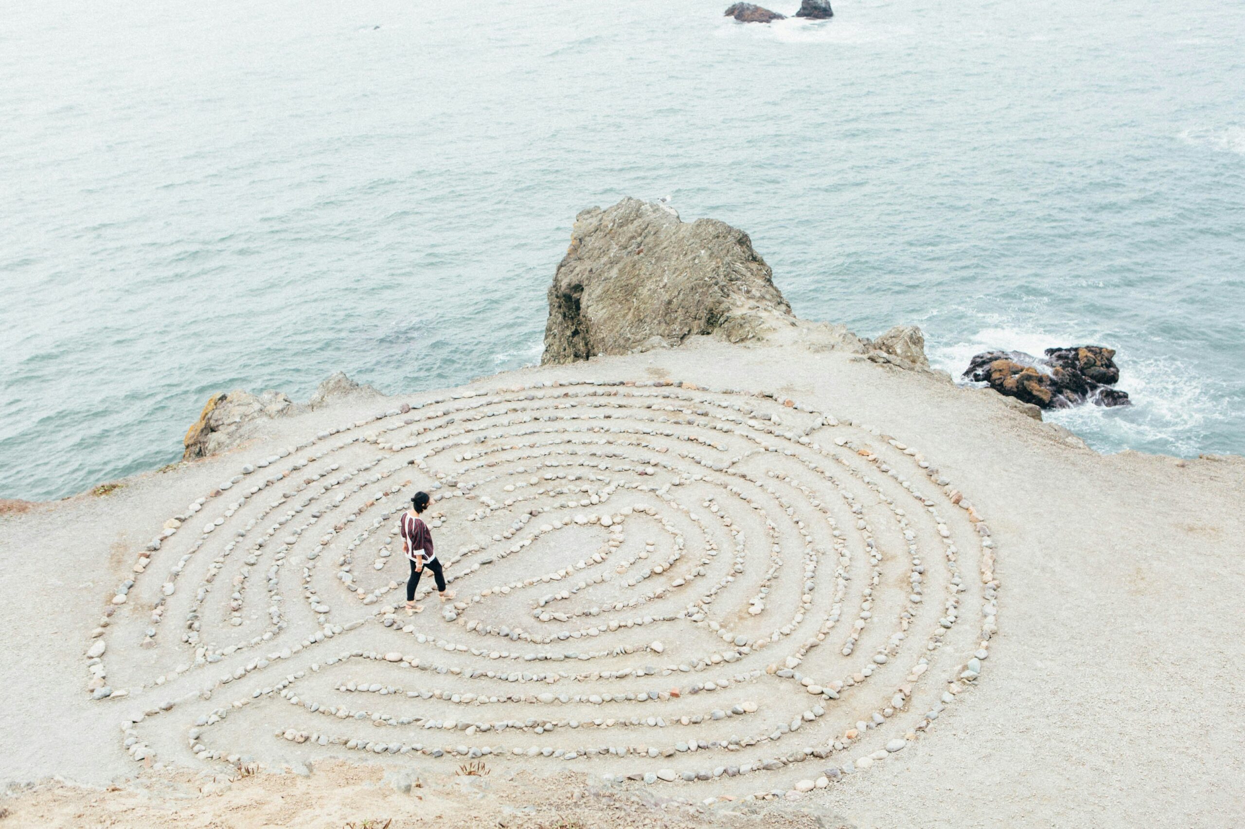 Der innere Weg — ein Labyrinth am Meer Vogelperspektive einer Person, die barfuß durch ein aus Steinen gelegtes Labyrinth am Meeresrand läuft — ein Symbol für die achtsame Suche nach dem eigenen Weg, innerer Einkehr und persönlicher Transformation